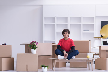 Image showing boy sitting on the table with cardboard boxes around him