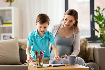 Image showing pregnant mother and son with workbook at home