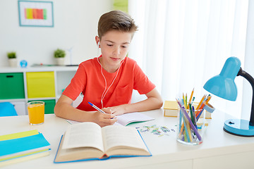 Image showing student boy in earphones writing to notebook