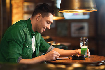 Image showing man with smartphone and green beer texting at bar