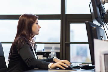 Image showing Casual businesswoman working in office, sitting at desk, typing on keyboard, looking at computer screen.