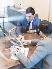 Image showing Two young businessmen using laptop computer at business meeting.