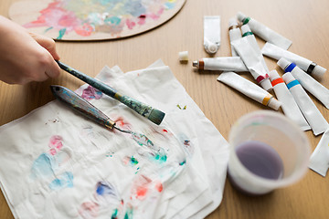 Image showing artist hand with paintbrush, paper and paint tubes