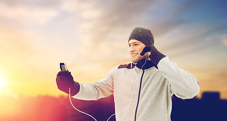 Image showing happy man with earphones and smartphone in winter