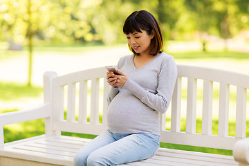 Image showing happy pregnant asian woman with smartphone at park
