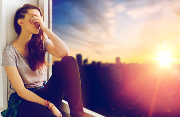 Image showing unhappy teenage girl sitting on windowsill