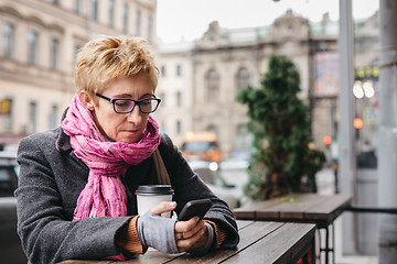 Image showing Woman browsing phone in outside cafe