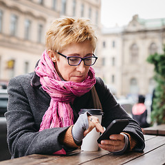 Image showing Woman browsing smartphone in outside cafe