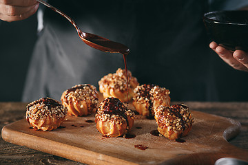 Image showing Decorating delicious homemade eclairs with chocolate and peanuts