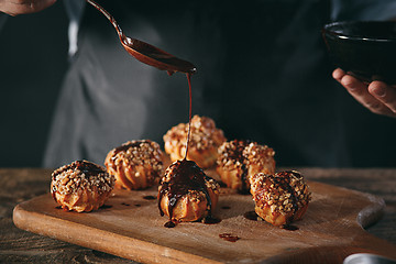 Image showing Decorating delicious homemade eclairs with chocolate and peanuts