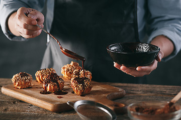 Image showing Decorating delicious homemade eclairs with chocolate and peanuts