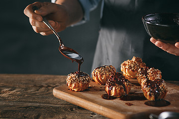 Image showing Decorating delicious homemade eclairs with chocolate and peanuts