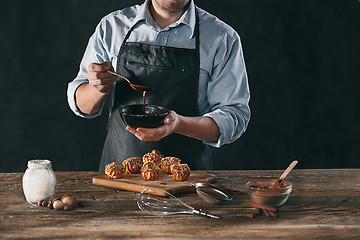 Image showing Decorating delicious homemade eclairs with chocolate and peanuts