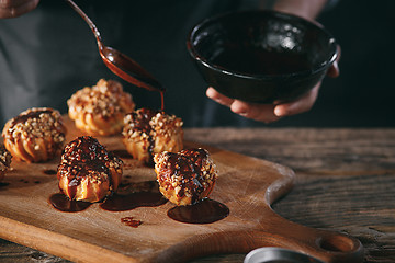 Image showing Decorating delicious homemade eclairs with chocolate and peanuts