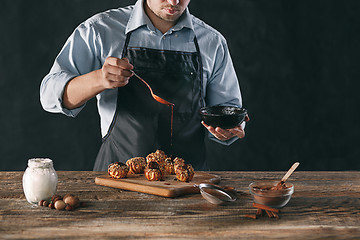 Image showing Decorating delicious homemade eclairs with chocolate and peanuts