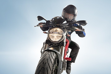 Image showing Biker in black jacket and helmet sitting on his sportive bike on blue background