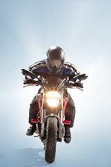 Image showing Biker in black jacket and helmet sitting on his sportive bike on blue background