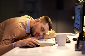 Image showing tired man sleeping on table at night office