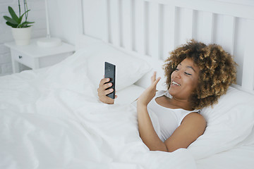 Image showing Smiling woman in bed talking online