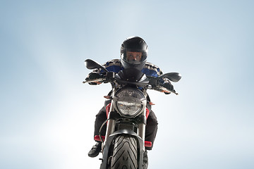 Image showing Biker in black jacket and helmet sitting on his sportive bike on blue background