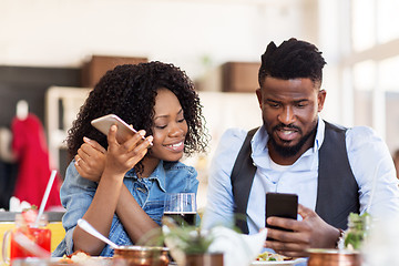 Image showing happy man and woman with smartphones at restaurant