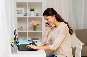 Image showing woman with laptop calling on smartphone at home