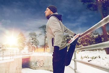 Image showing sports man stretching leg at fence in winter