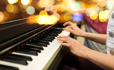 Image showing close up of woman hands playing piano over lights