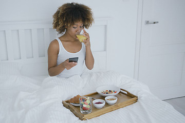 Image showing Woman with phone enjoyin breakfast in bed