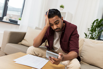 Image showing confused man with papers and calculator at home