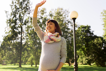 Image showing happy pregnant asian woman waving hand at park