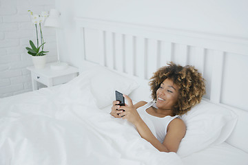 Image showing Smiling woman relaxing with phone in bed