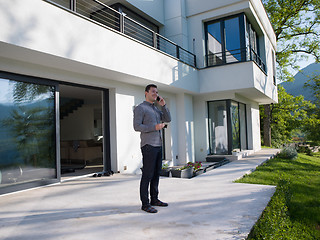 Image showing man using mobile phone in front of his luxury home villa