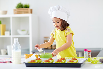 Image showing little girl in chefs toque baking muffins at home