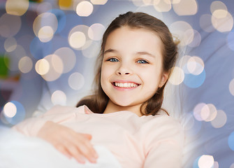 Image showing happy smiling girl lying awake in bed over lights