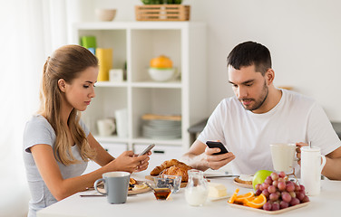 Image showing couple with smartphones having breakfast at home