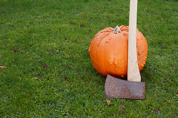 Image showing Axe leans against large orange pumpkin