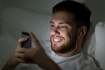 Image showing man with smartphone and earphones in bed at night