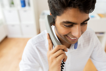 Image showing happy businessman calling on desk phone at office