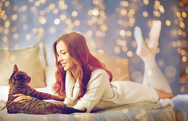 Image showing happy young woman with cat lying in bed at home