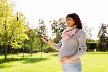 Image showing happy pregnant asian woman taking selfie at park