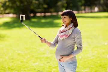 Image showing happy pregnant asian woman taking selfie at park