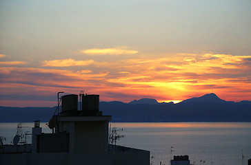 Image showing Beautiful sunset on the sea and top of roofs with antennas