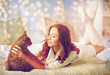 Image showing happy young woman with cat lying in bed at home