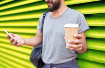 Image showing man with coffee cup and smartphone over wall