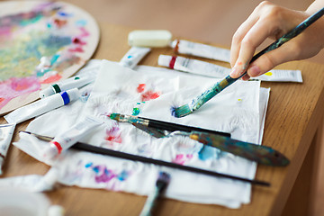 Image showing artist hand with paintbrush, paper and paint tubes