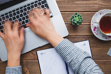 Image showing Man working on laptop placed on wooden desk