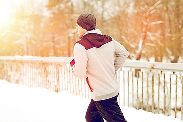 Image showing man in earphones running along winter bridge
