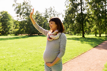 Image showing happy pregnant asian woman waving hand at park