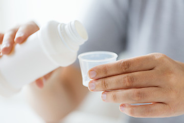 Image showing woman pouring syrup from bottle to medicine cup